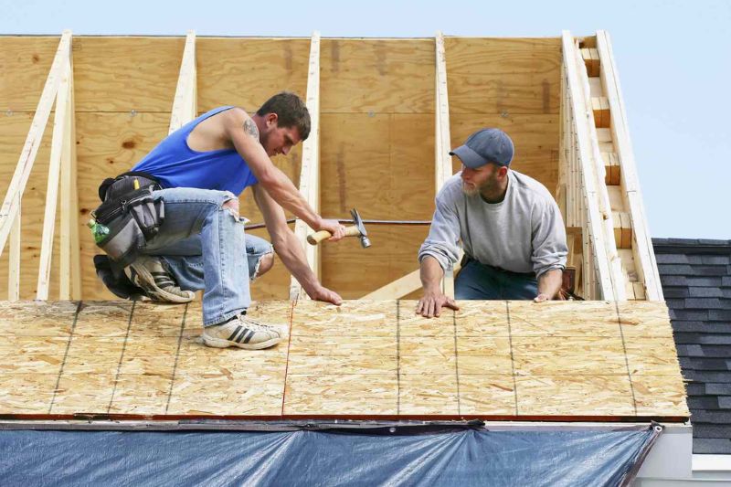 Two workers performing roof replacement on a wooden frame, showcasing their expertise in Naperville.