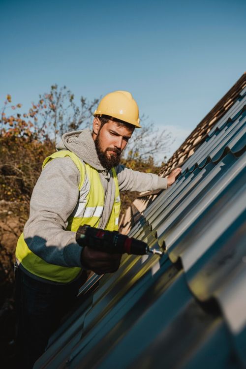 A professional in a hard hat and safety vest is actively working on a metal roof for a roofing service in Naperville.