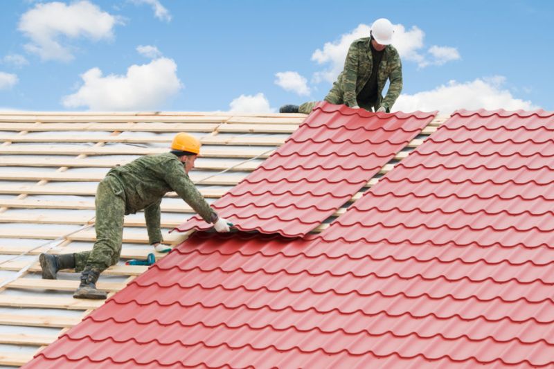 Two workers on a roof in Naperville, applying red metal tiles during a reroofing project.
