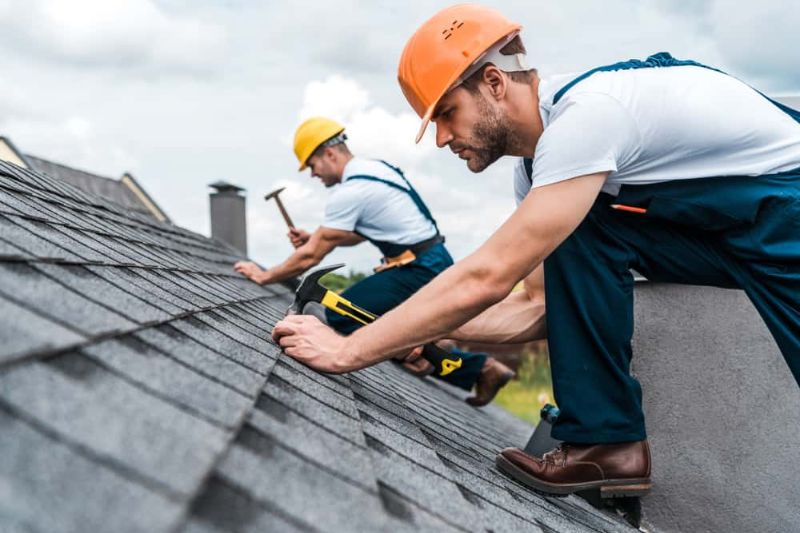 Two workers engaged in roof maintenance in Naperville, utilizing hammers to install or repair roofing materials.