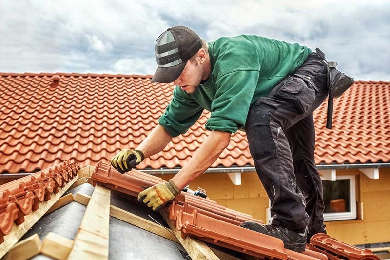 A man is engaged in roofing work, laying red tiles, highlighting roofing services available in Naperville.