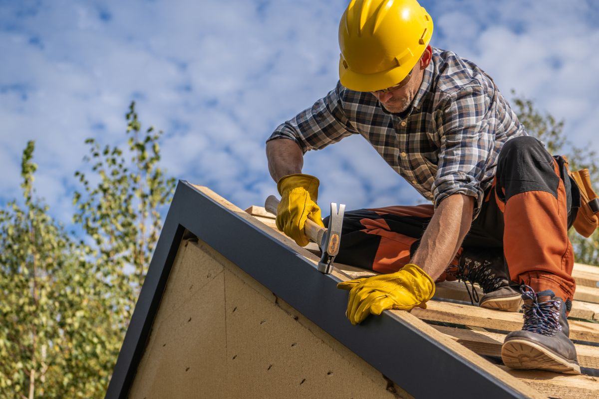  A worker in a hard hat and yellow safety vest is engaged in roofing activities, focusing on safety and precision on the roof.