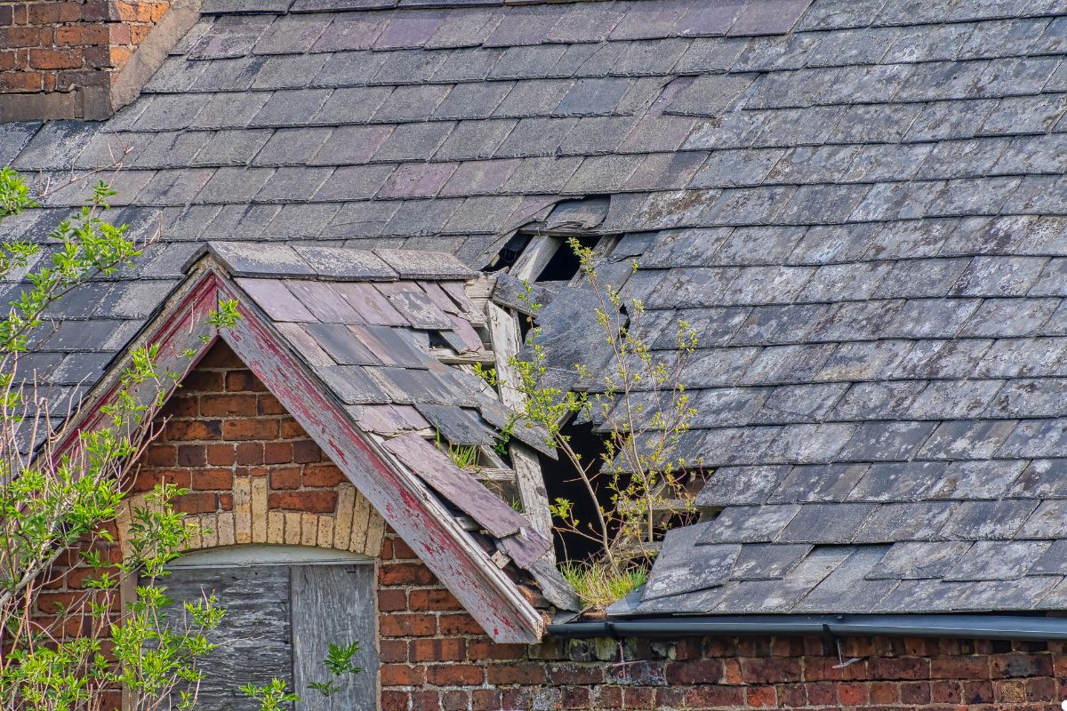 A brick house featuring a damaged roof, with missing shingles and structural issues evident.